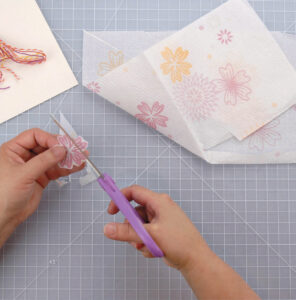 person using scissors to cut out a flower from a napkin